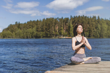 Fototapeta na wymiar Woman practicing yoga with namaste behind the back. fitness lifestyle at the outdoors water background. Sunny day in pine forest. copy space
