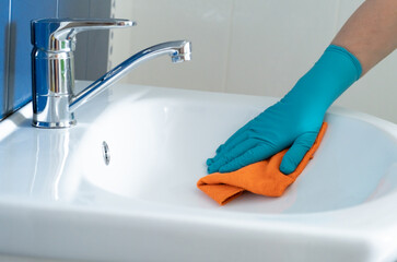 Female hand in protective gloves wiping a sink. Cleaning concept