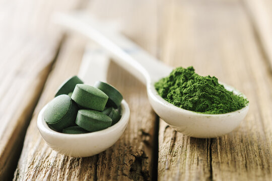Two white spoons with pills and chlorella powder on old boards. Spoons with chlorella or spirulina.