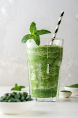 Glass of smoothies with addition of chlorella or spirulina with mint on a grey concrete background.