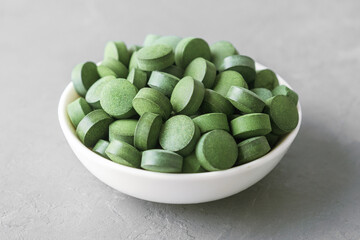 A cup of chlorella or spirulina tablets on grey concrete.