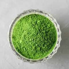 Shredded chlorella or spirulina in a glass cup on grey concrete. Top view.