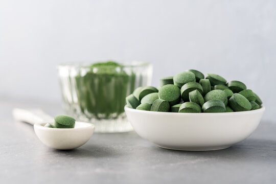 Chlorella or spirulina in the form of tablets and powder on a gray concrete background.
