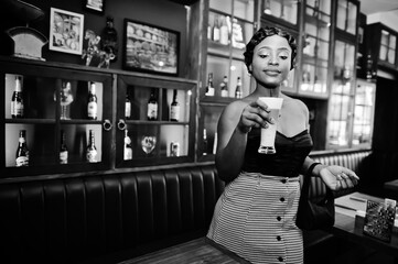 Portrait of african american woman, retro hairstyle posing at restaurant with cup of latte.