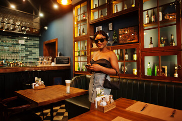 Portrait of african american woman, retro hairstyle posing at restaurant with cup of latte.