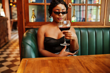 Portrait of african american woman, retro hairstyle posing at restaurant with glass of wine.