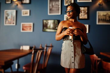 Portrait of african american woman, retro hairstyle posing at restaurant with cup of latte.