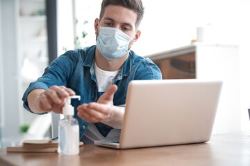 Fototapeta na wymiar Coronavirus. Man working from home wearing protective mask. Cleaning his hands with sanitizer gel