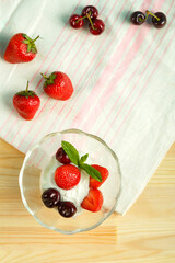 Ice cream dessert with strawberries and cherries in a gourd on a wooden table next to scattered berries.