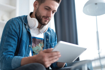 Attractive young man is using a tablet and smiling while lying on sofa at home.