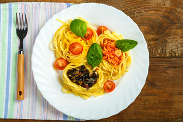 Plate on a napkin nest pasta stuffed with assorted pasta paste, cheese with cherry and fried mushrooms next to a fork.