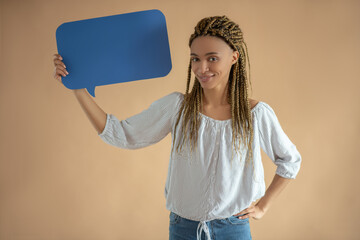 Happy young African American female holding blue dialogue cloud with one hand, another hand on her...