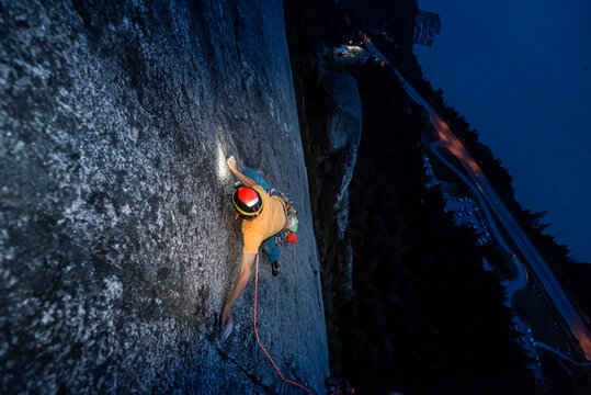 Top view man rock climbing at night above the sea and highway