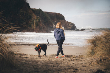 A woman with an infant is playing with a dog on the Californian beach
