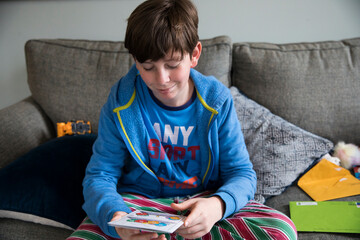 Smirking Teen Boy Reads Birthday Card While Sitting on Couch in Pjs