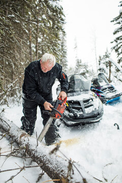 Snowmobiler using chainsaw to clear trails