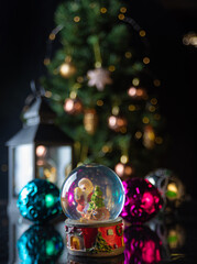 Christmas scene with tree, lights and snow globe. Selective focus on black background.