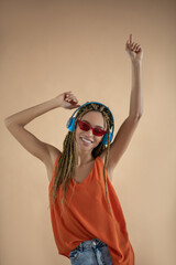 Smiling young African American female wearing headphones, raising her hands, dancing