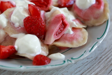 Dumplings with starwberries on plate close up decorated with fresh strawberries and cream