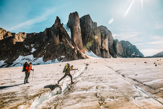 Mounatineer crosses a glacial crevasse on a sunny day, Baffin Island.