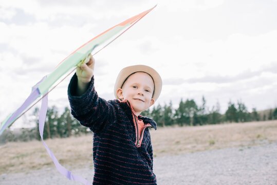 young boy holding a kite smiling whilst outside on a sunny day