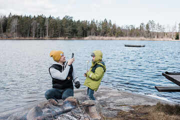 man taking a picture of his son whilst camping eating marshmallows