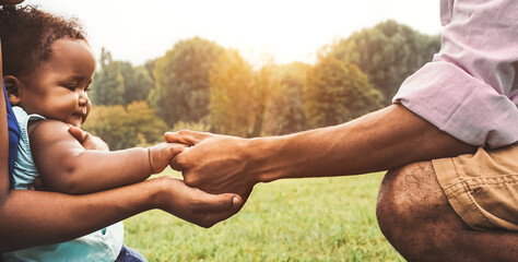 Happy African family having fun together in public park - Black father and mother holding hand with...