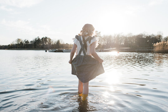 young girl walking through water in a pretty dress at sunset