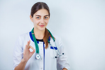 Portrait of an attractive young female doctor in white coat. White background. Copy space. Young cheerful happy woman doctor posing isolated over white wall background with stethoscope.