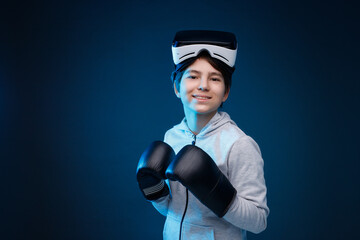 Portrait of young boy in glasses of virtual reality, boxing gloves and hoodie on dark background. Augmented reality, future technology concept. VR. Blue neon light.