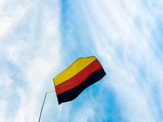 Famous German black, red and yellow flag on flag pole against blue sky. National symbol of Germany
