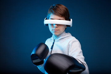 Portrait of young boy in glasses of virtual reality, boxing gloves and hoodie on dark background. Augmented reality, future technology concept. VR. Blue neon light.