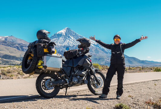 Woman standing next to touring motorbike. Lanin volcano in the back