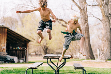 Two boys jumping off picnic table