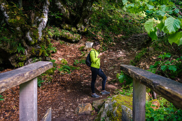 Fototapeta premium Young woman looking at her mobile phone while hiking in Asturias, wooden bridge in close up