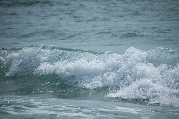 Small cresting wave in the Atlantic Ocean on the coast. Blue green ocean waves with sea foam and salt water spray. Beach travel photos.