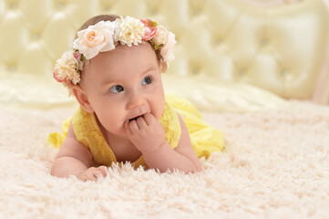 Cute little baby girl in wreath on bed