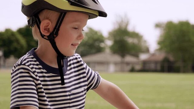 Cute little boy is riding bike on the sidewalk. Child in a helmet, orange kids bicycle. Childhood memories, outdoors activities. Suburban street, daytime