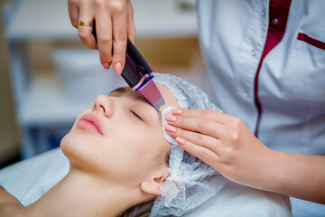 Woman receiving ultrasonic facial exfoliation at cosmetology salon. Procedure clearing clogged...