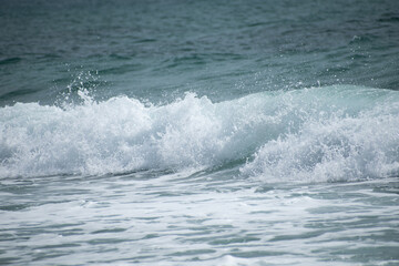 Small cresting wave in the Atlantic Ocean on the coast. Blue green ocean waves with sea foam and salt water spray. Beach travel photos.