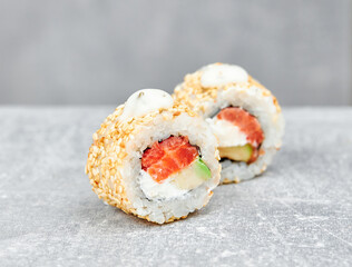 two slices of sushi rolls uramaki with cheese, salmon, avocado, sprinkled with white sesame seeds