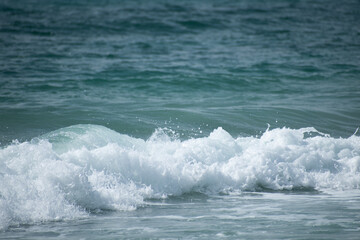 Small cresting wave in the Atlantic Ocean on the coast. Blue green ocean waves with sea foam and salt water spray. Beach travel photos.