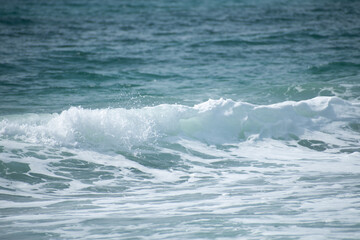 Small cresting wave in the Atlantic Ocean on the coast. Blue green ocean waves with sea foam and salt water spray. Beach travel photos.