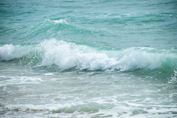 Small cresting wave in the Atlantic Ocean on the coast. Blue green ocean waves with sea foam and salt water spray. Beach travel photos.