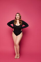 Fototapeta na wymiar Plus size model girl in black bodysuits posing at the pink background, isolated.