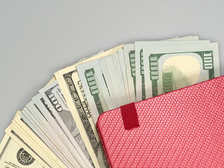 Pink notepad laying on fan style layout of one hundred dollar banknotes, copy space