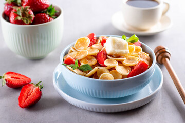 Blue Bowl for breakfast with Pancake cereals served with strawberries, butter and honey on gray background. Copy space