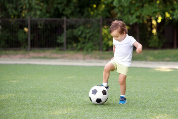 Toddler boy stopping soccer ball at football field. Little football player with raised leg ready to...