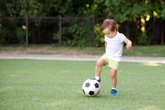 Toddler boy stopping soccer ball at football field. Little football player with raised leg ready to kick ball back in game. Young athlete and active childhood concept. Copy space