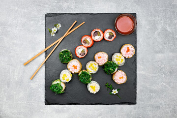 Fresh fish sushi set with side dishes on a black graphite board and gray background